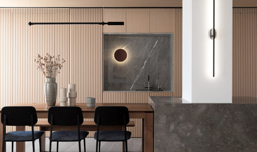 Modern dining area with fluted wood wall panels, wooden dining table, black dining chairs, marble feature wall, concealed sink, and minimalist lighting