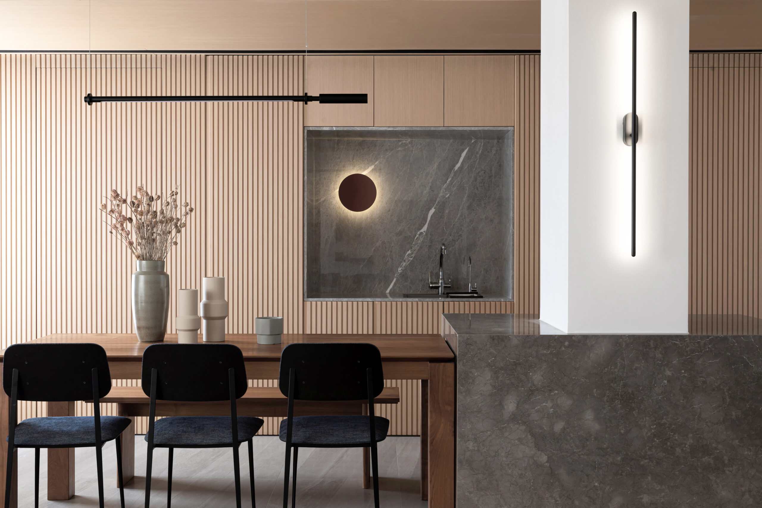 Modern dining area with fluted wood wall panels, wooden dining table, black dining chairs, marble feature wall, concealed sink, and minimalist lighting