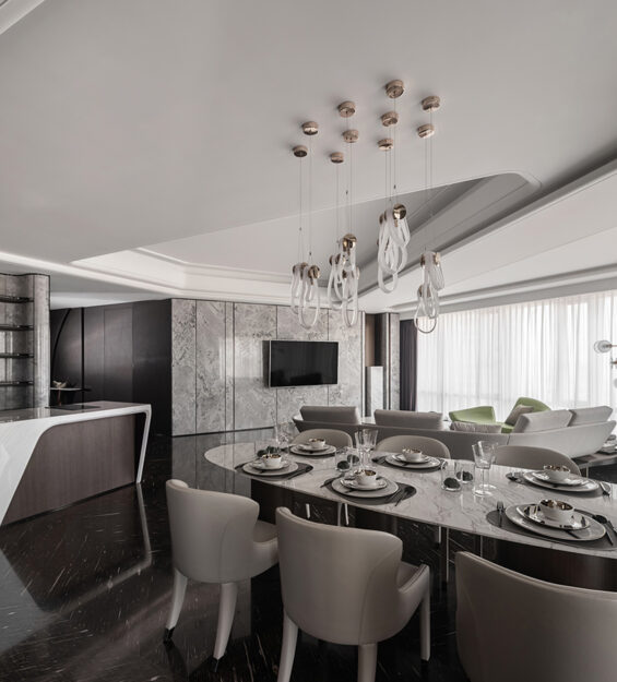 Luxury open-plan dining and living area with marble flooring, oval dining table, modern chandelier, built-in bar counter, and floor-to-ceiling windows