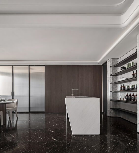 Ultra-luxury modern interior with marble kitchen island, dark wood paneling, built-in bar shelving, black marble flooring, and elegant dining area under recessed ceiling lighting.