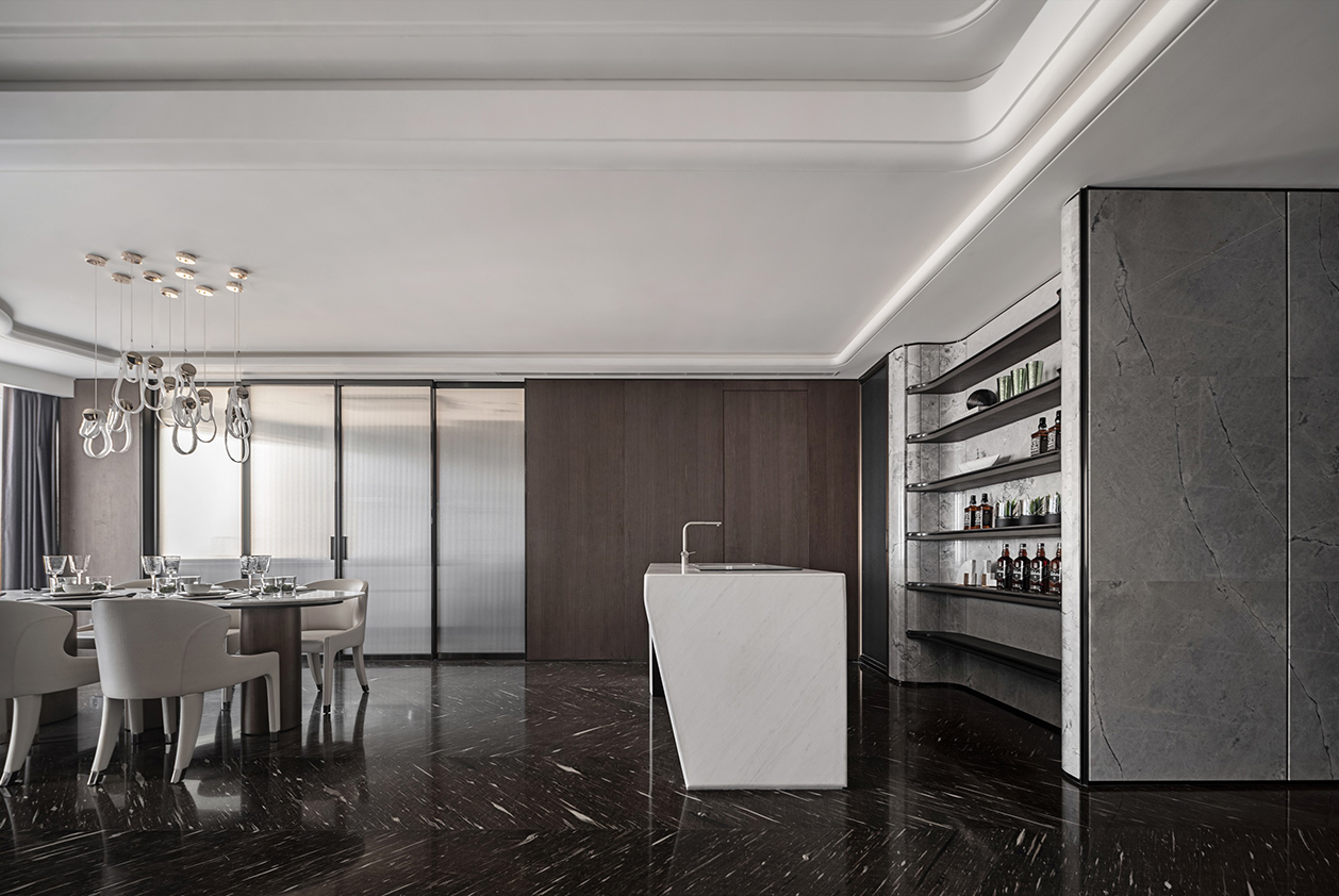 Ultra-luxury modern interior with marble kitchen island, dark wood paneling, built-in bar shelving, black marble flooring, and elegant dining area under recessed ceiling lighting.