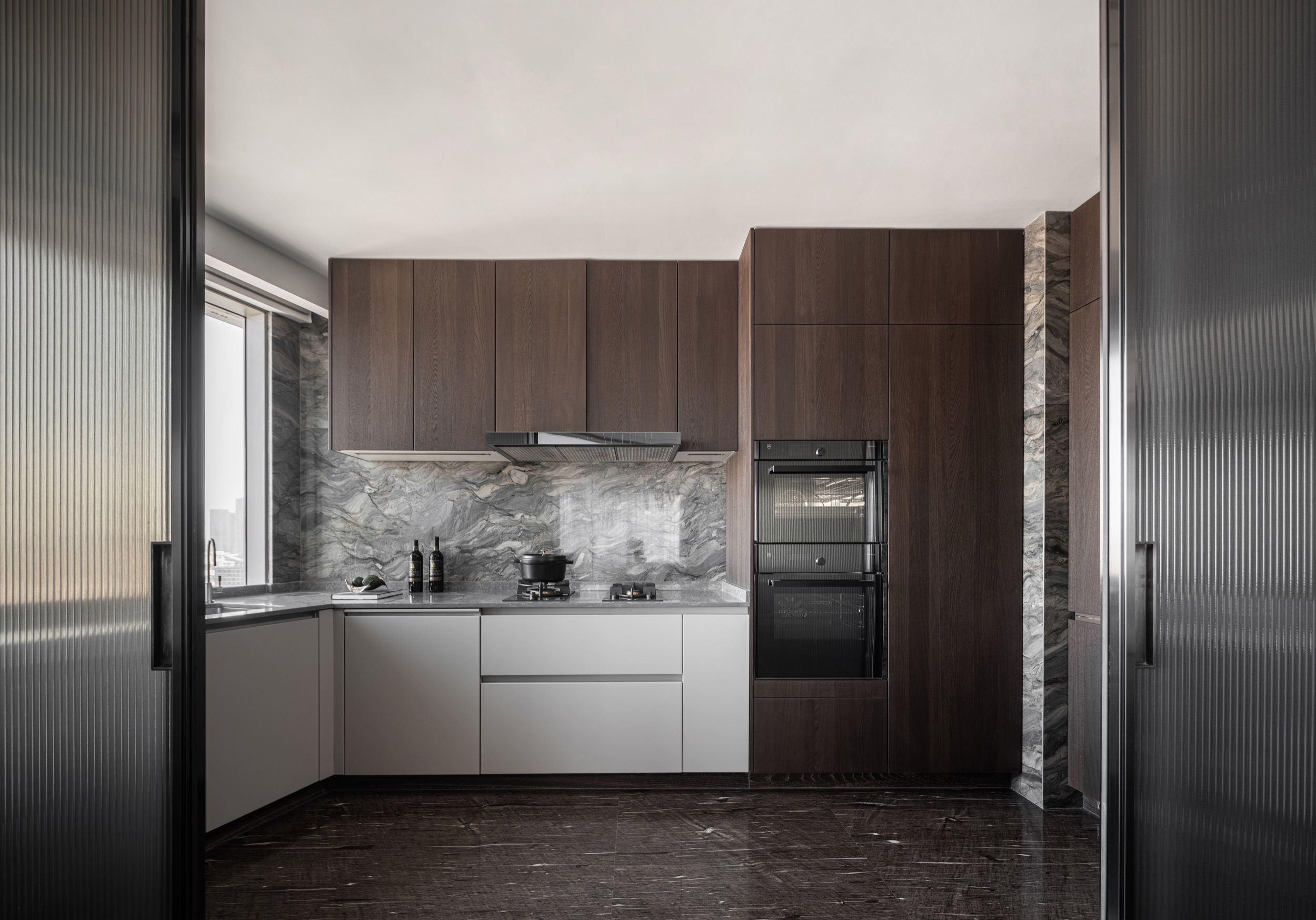 Modern kitchen design with dark wood cabinetry, marble backsplash, built‑in oven, and minimalist grey countertops.
