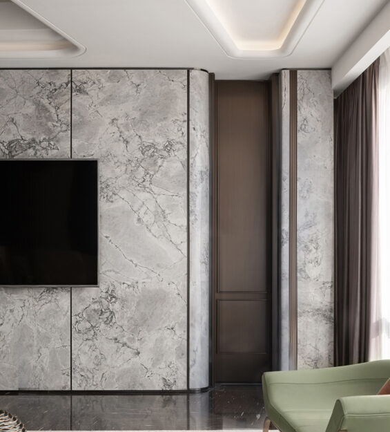 Contemporary living room with a marble feature wall and wall‑mounted TV, light‑coloured sofa, round and rectangular coffee tables, green lounge chairs, and floor‑to‑ceiling sheer curtains.