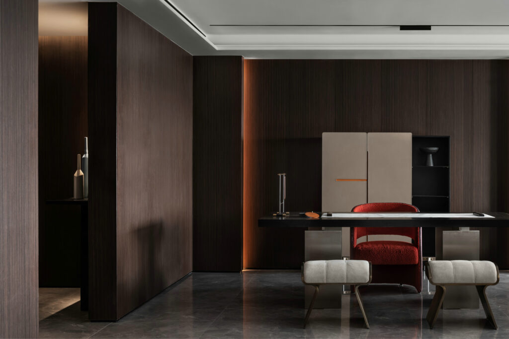 Luxury modern home office interior with dark wood wall panels, minimalist desk, red upholstered chair, concealed lighting, and marble flooring