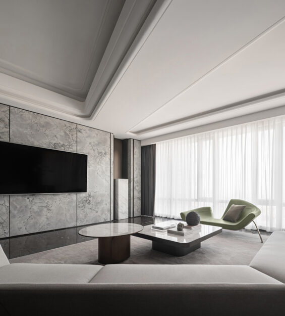 Contemporary living room with a marble feature wall and wall‑mounted TV, light‑coloured sofa, round and rectangular coffee tables, green lounge chairs, and floor‑to‑ceiling sheer curtains.