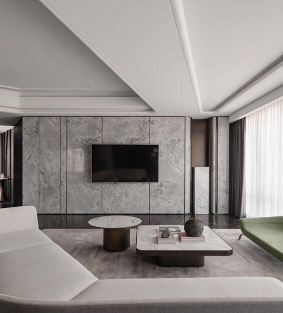 Contemporary living room with a marble feature wall and wall‑mounted TV, light‑coloured sofa, round and rectangular coffee tables, green lounge chairs, and floor‑to‑ceiling sheer curtains.