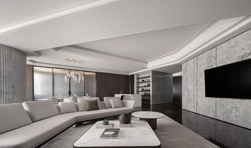 Contemporary living room with a marble feature wall and wall‑mounted TV, light‑coloured sofa, round and rectangular coffee tables, green lounge chairs, and floor‑to‑ceiling sheer curtains.