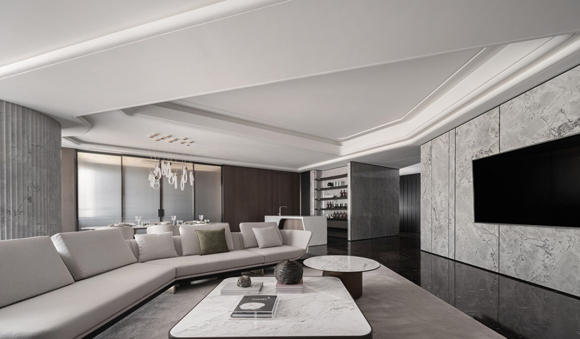 Contemporary living room with a marble feature wall and wall‑mounted TV, light‑coloured sofa, round and rectangular coffee tables, green lounge chairs, and floor‑to‑ceiling sheer curtains.