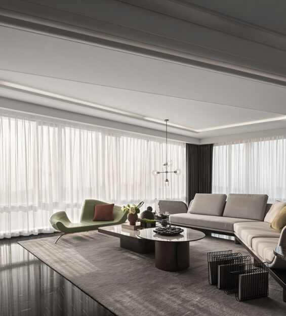 Contemporary living room with a marble feature wall and wall‑mounted TV, light‑coloured sofa, round and rectangular coffee tables, green lounge chairs, and floor‑to‑ceiling sheer curtains.